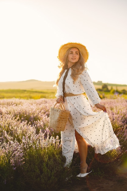 Mujer provenzal relajante en campo de lavanda. Dama con un vestido blanco. Chica con sombrero de paja y canasta.