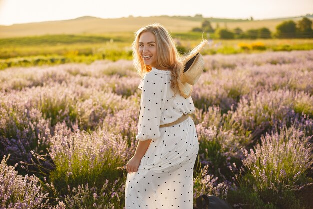 Mujer provenzal relajante en campo de lavanda. Dama con un vestido blanco. Chica con sombrero de paja.