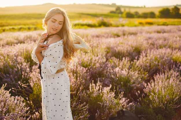 Mujer provenzal relajante en campo de lavanda. Dama con un vestido blanco. Chica con sombrero de paja.