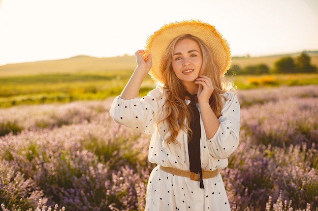 Mujer provenzal relajante en campo de lavanda. Dama con un vestido blanco. Chica con sombrero de paja.