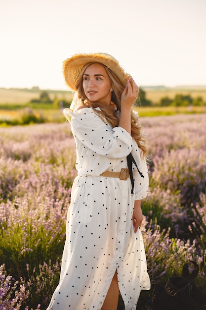 Mujer provenzal relajante en campo de lavanda. Dama con un vestido blanco. Chica con sombrero de paja.