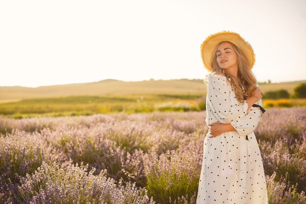 Mujer provenzal relajante en campo de lavanda. Dama con un vestido blanco. Chica con sombrero de paja.