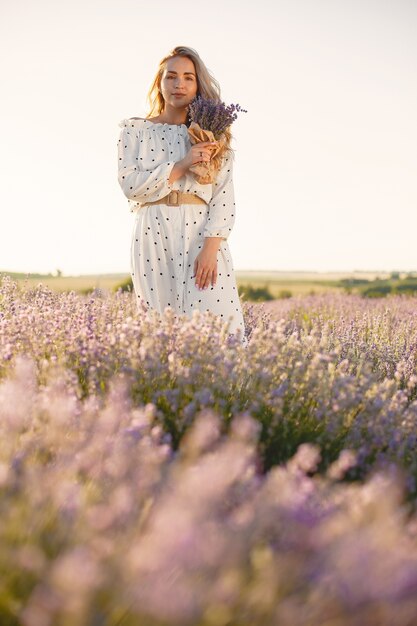 Mujer provenzal relajante en campo de lavanda. Dama con un vestido blanco. Niña con bouquete de flores.