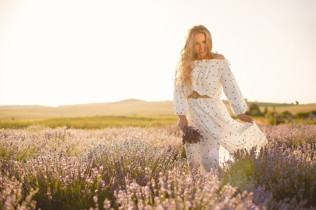 Mujer provenzal relajante en campo de lavanda. Dama con un vestido blanco. Niña con bouquete de flores.