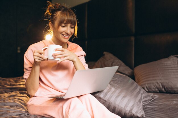 Mujer en pygama trabajando en laptop en cama