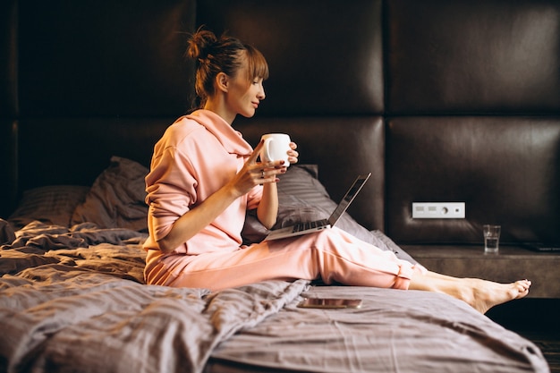 Mujer en pygama trabajando en laptop en cama