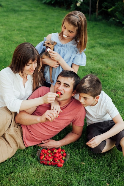 Foto gratuita mujer que alimenta la fresa al marido mientras que se sienta con sus niños en hierba