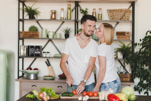 Mujer que ama a su novio que corta el tomate rojo con el cuchillo en cocina