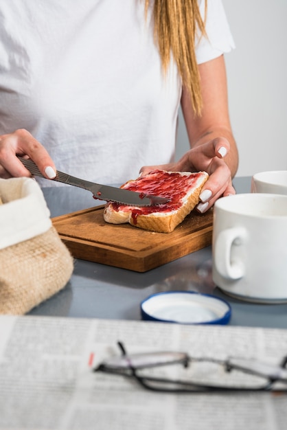 Mujer que aplica el atasco en la rebanada de pan en la mesa de desayuno