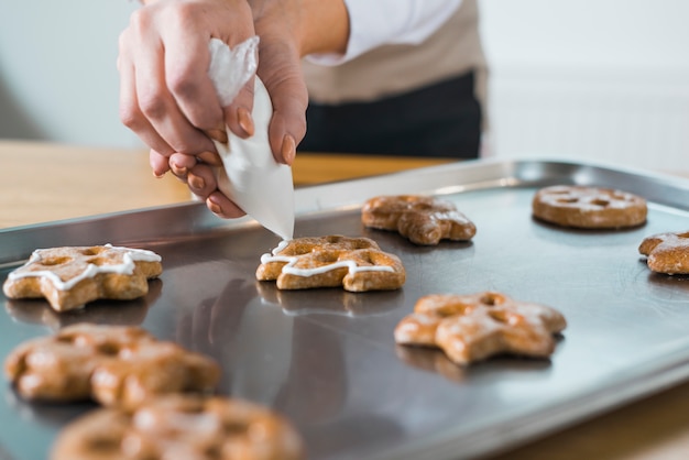 Mujer que aplica la crema a las galletas frescas de la Navidad en la bandeja