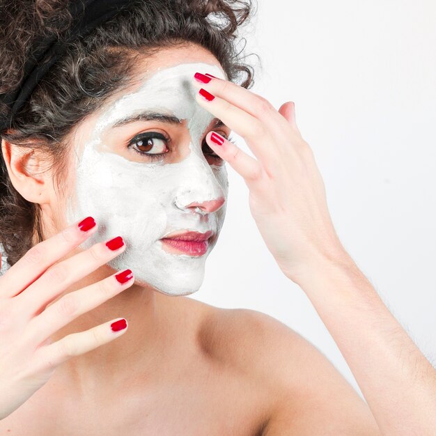 Mujer que aplica la mascarilla en su cara contra el fondo blanco