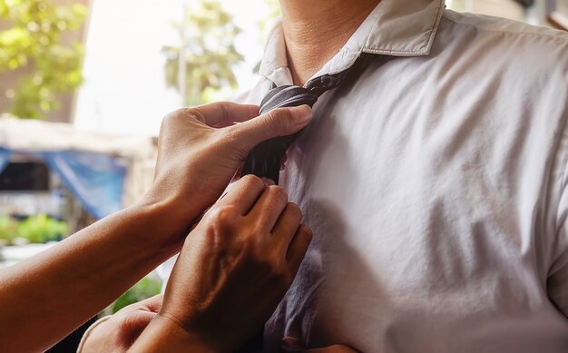 Mujer que ayuda a su marido a atar su corbata antes de ir a trabajar. Color de Vntage, foco selectivo. Concepto de negocio.