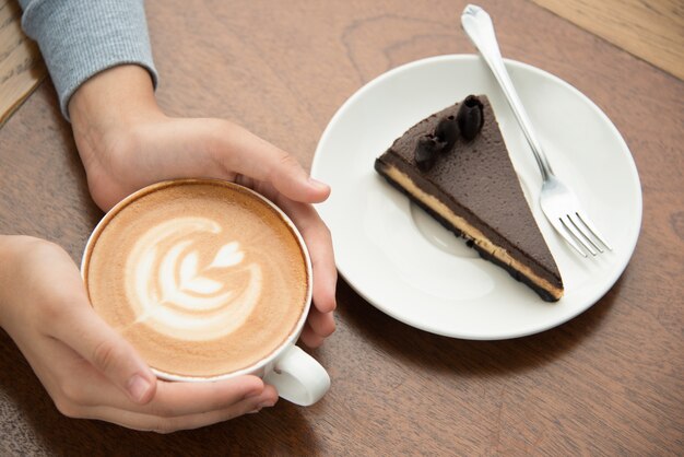 Mujer que bebe el cappuccino y que come la torta