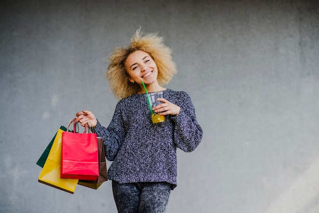 Mujer que camina con la bebida y las bolsas