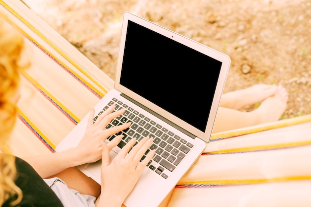 Mujer que charla en la computadora portátil en hamaca