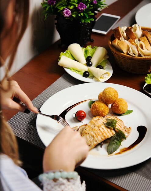 Mujer que come Filete De Salmón Al Horno Con Patatas Y Rollitos De Queso, Y Mezcla De Verduras.