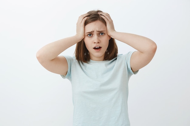 La mujer que comienza el pánico no puede cumplir con el plazo a tiempo. Retrato de desesperada malestar y triste linda chica preocupada tomados de la mano en el cabello abriendo la boca y frunciendo el ceño comparando sentirse preocupado y nervioso