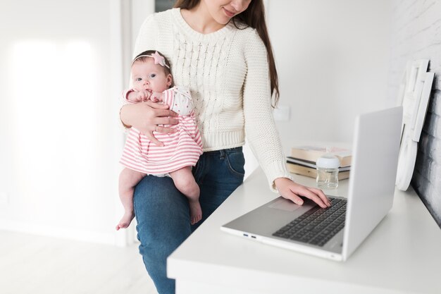 Mujer que controla la computadora portátil con el bebé