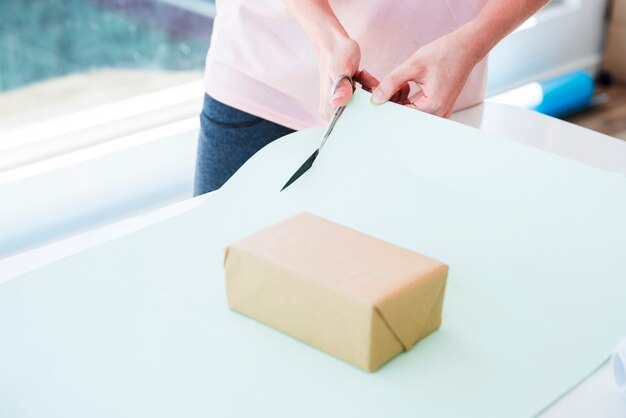 Mujer que corta el papel de la tarjeta con una tijera para envolver la caja de regalo