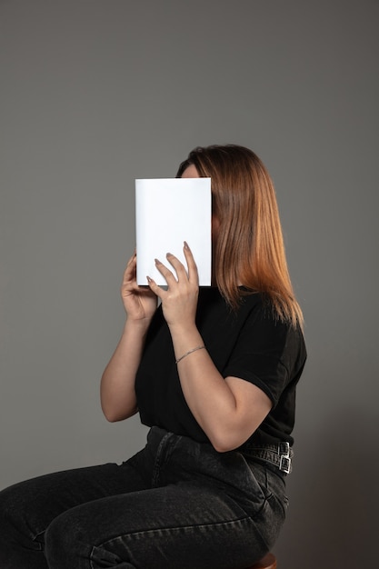 mujer que cubre la cara con el libro mientras lee en la pared gris. Celebrando, educación, arte, disfrutando del concepto de nuevos personajes.