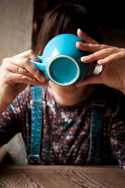 Mujer que cubre la cara con la taza de cerámica azul mientras bebe café