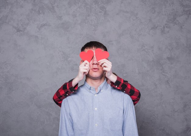 Mujer que cubre ojos de hombre con corazones de papel rojo