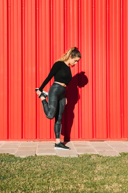 Mujer que estira la pierna cerca de la pared roja