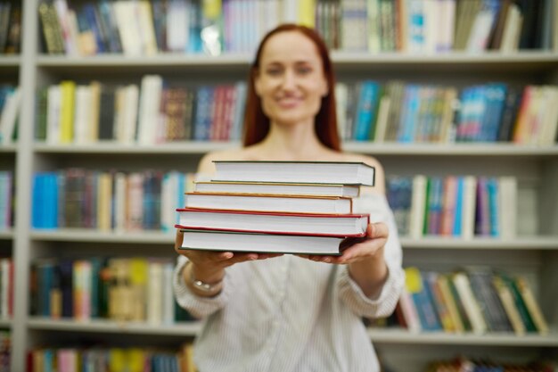 Mujer que estira la pila de libros a la cámara