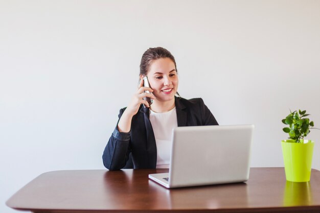 Mujer que habla el teléfono en la computadora portátil