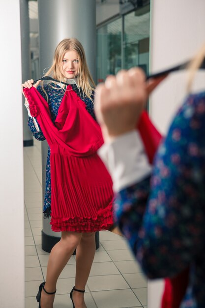 Mujer que intenta el vestido rojo que hace compras para la ropa.