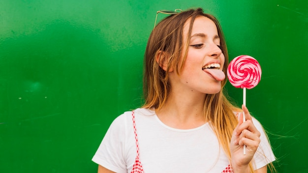 Mujer que lame la piruleta roja y rosada que se opone a fondo verde