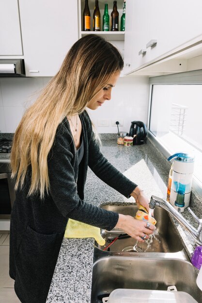 Mujer que lava el envase en fregadero de cocina