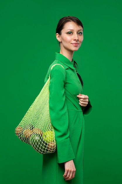 Mujer que lleva una bolsa de malla con manzanas, aguacate y kiwi.