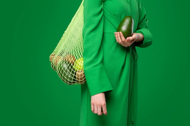 Mujer que lleva una bolsa de malla con manzanas, aguacate y kiwi.