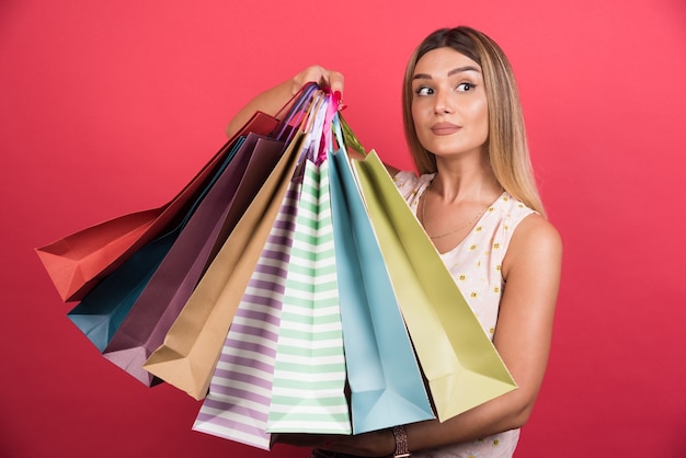 Foto gratuita mujer que lleva bolsas de la compra con expresión neutra en la pared roja.