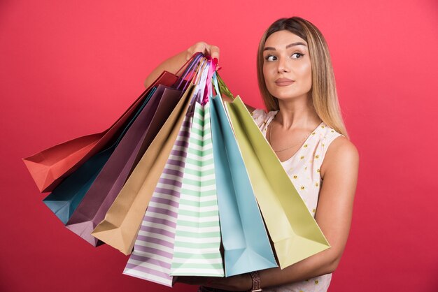 Mujer que lleva bolsas de la compra con expresión neutra en la pared roja.