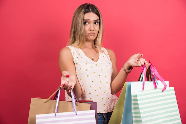 Mujer que llevaba bolsas de la compra con expresión triste en la pared roja.