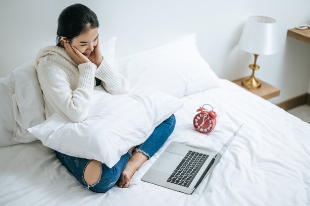 Una mujer que llevaba una camisa blanca en la cama y jugando felizmente portátil.