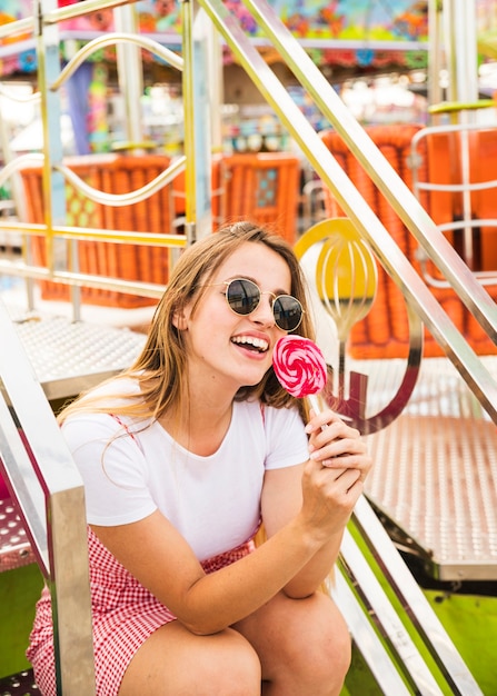 Mujer que llevaba gafas de sol sentado en el parque de atracciones con lollipop