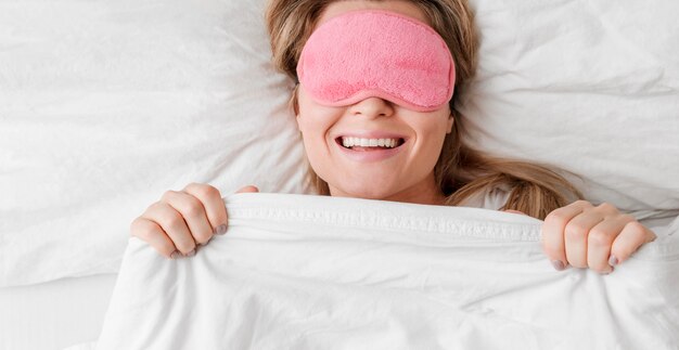 Mujer que llevaba una máscara para dormir en sus ojos y sonrisas