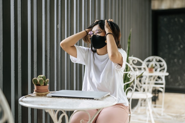 Una mujer que llevaba una máscara jugando una computadora portátil y ambas manos sosteniendo la cabeza
