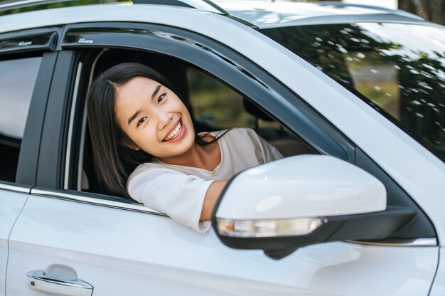 Una mujer que maneja el auto sonríe alegremente y abre la ventana.