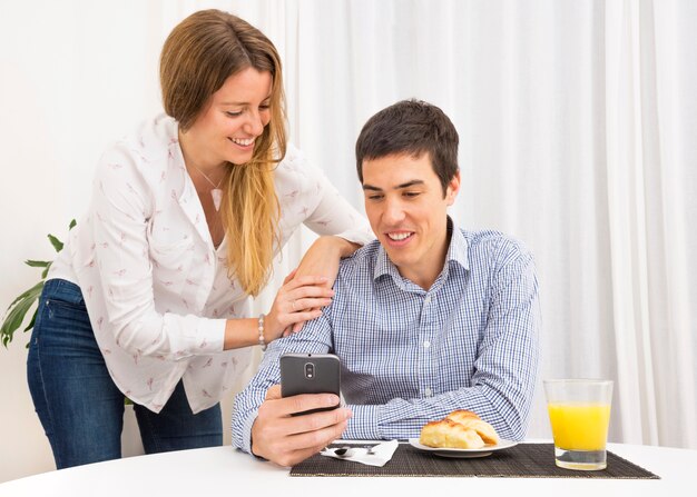 Mujer que mira al hombre que desayuna usando el teléfono móvil