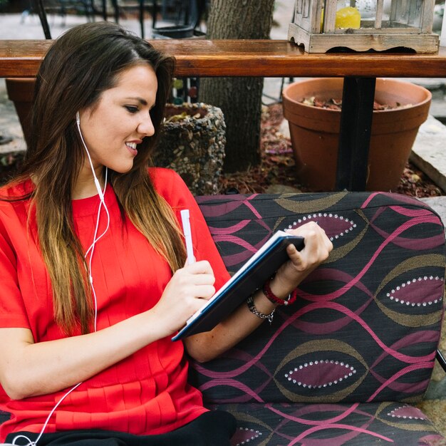 Mujer que mira el diario que escucha la música en el auricular