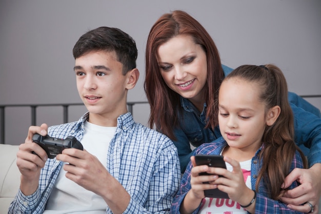 Mujer que mira a la muchacha y al adolescente que usan tecnologías