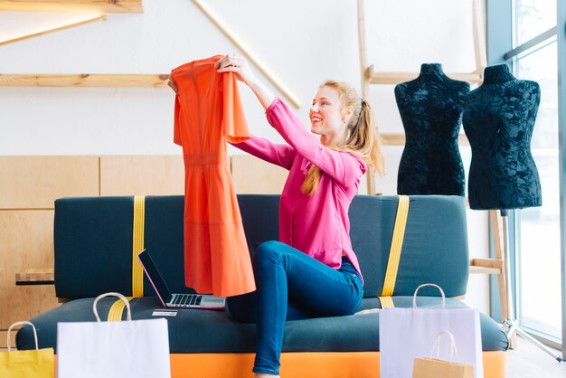 Mujer que mira el nuevo vestido cerca de la computadora portátil