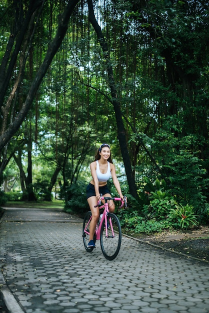Mujer que monta una bicicleta de carretera en el parque. Retrato de la mujer hermosa joven en la bici rosada.