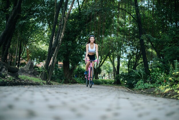 Mujer que monta una bicicleta de carretera en el parque. Retrato de la mujer hermosa joven en la bici rosada.