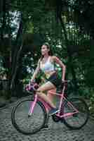 Foto gratuita mujer que monta una bicicleta de carretera en el parque. retrato de la mujer hermosa joven en la bici rosada.