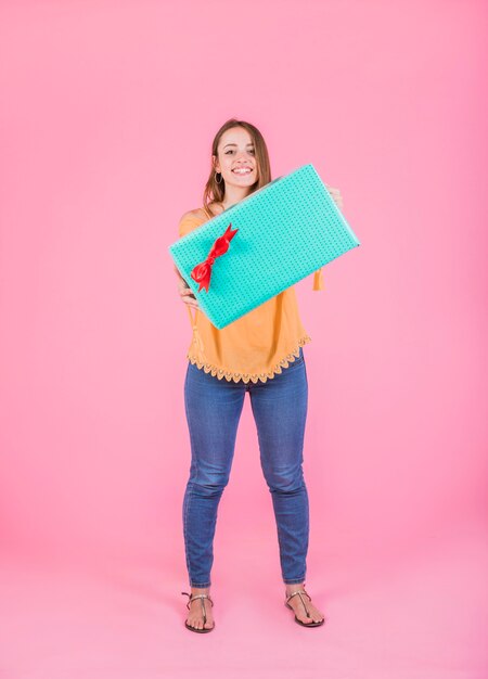 Mujer que muestra la caja de regalo envuelta que se opone a fondo rosado